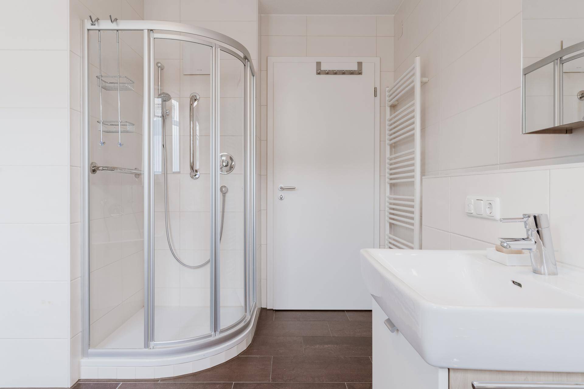 Modernes Badezimmer mit Duschkabine, Waschbecken und beheiztem Handtuchhalter.