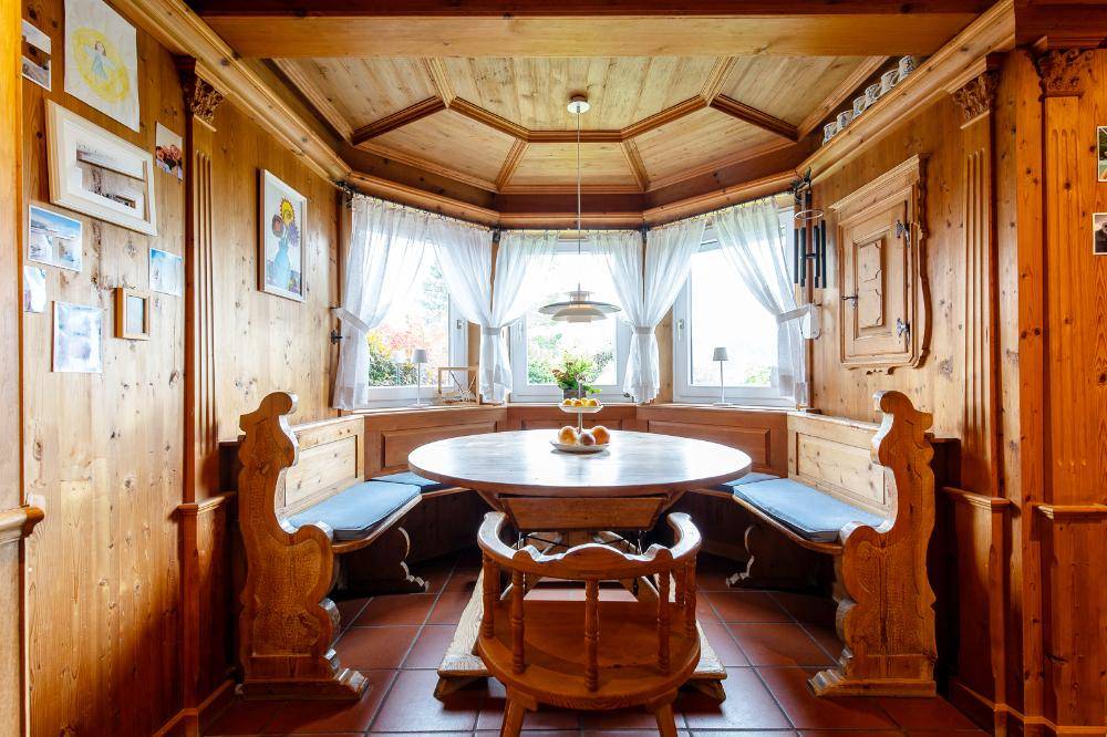 Traditioneller Essbereich mit Holztäfelung, Eckbank und einem runden Holztisch am Erkerfenster.