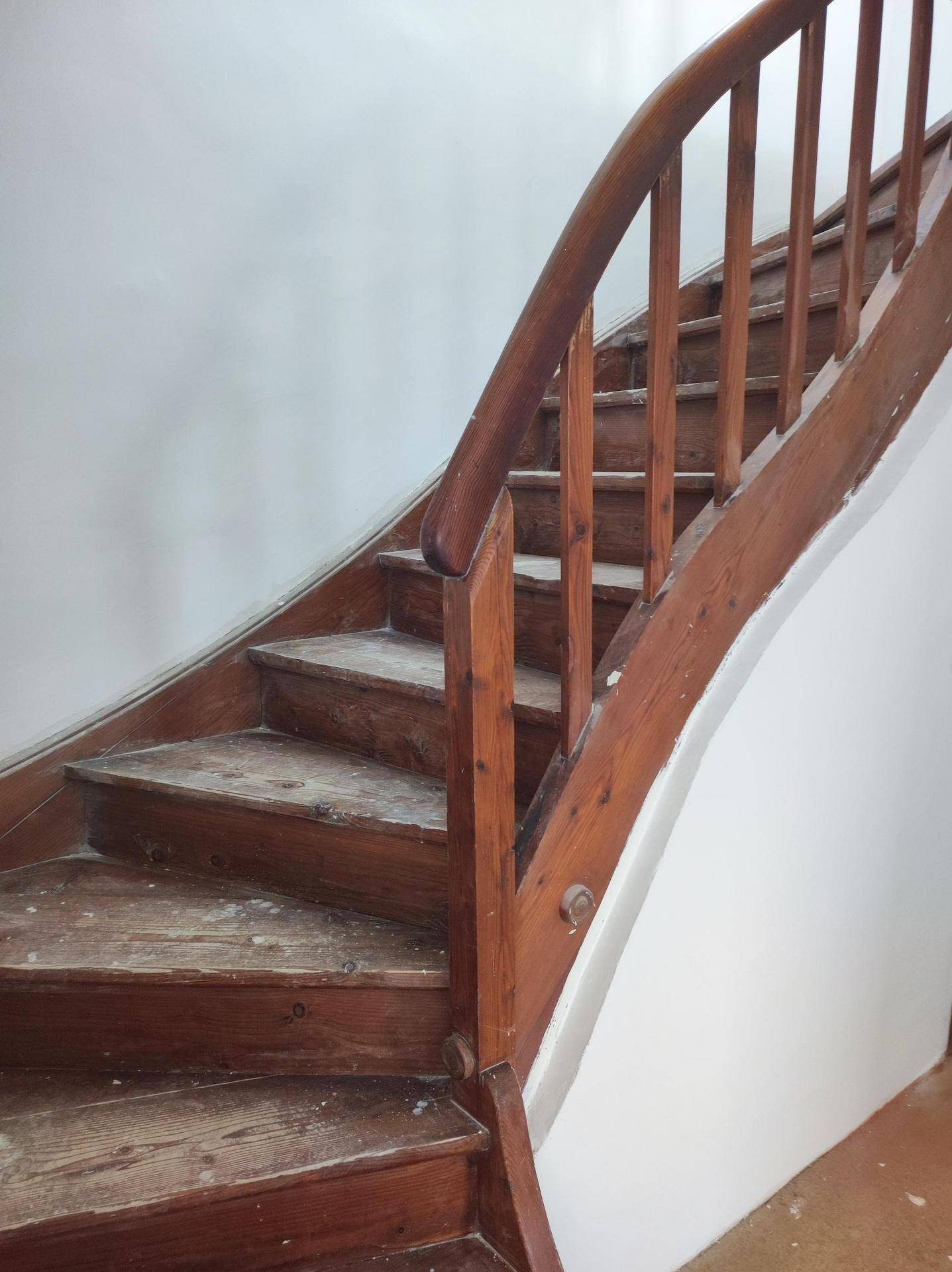 Alte Holztreppe mit gedrechseltem Geländer, die in einem Flur nach oben führt.