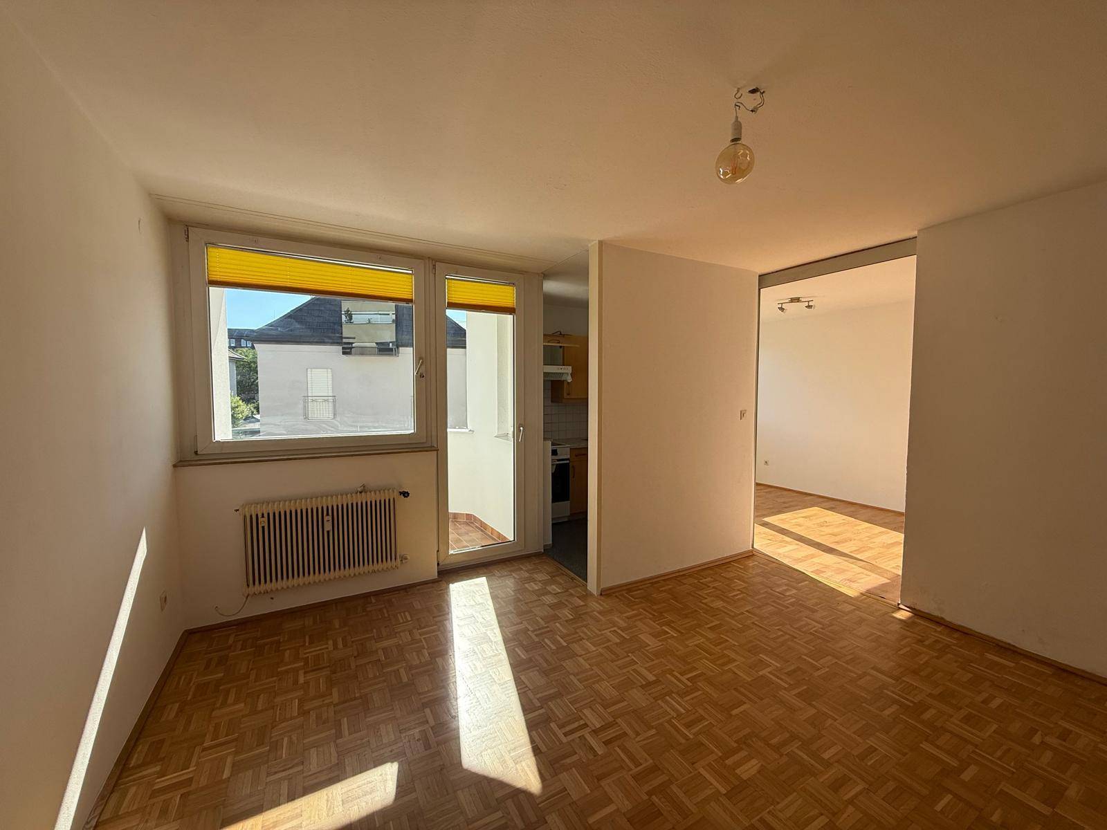 Heller Wohnbereich mit Parkettboden und Zugang zu einem kleinen Balkon.