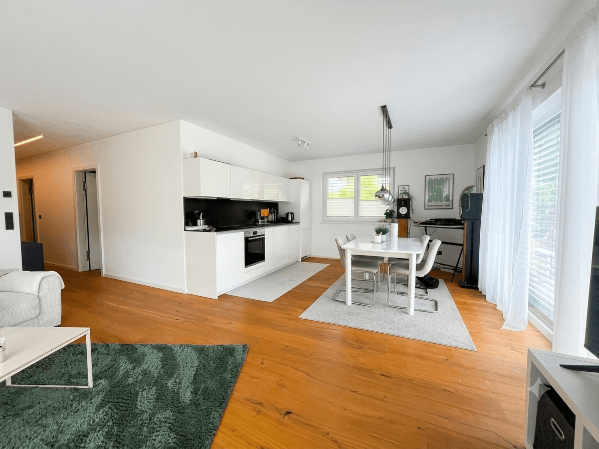Geräumiger Wohn-Essbereich mit integrierter, moderner Küche und Zugang zum Balkon.