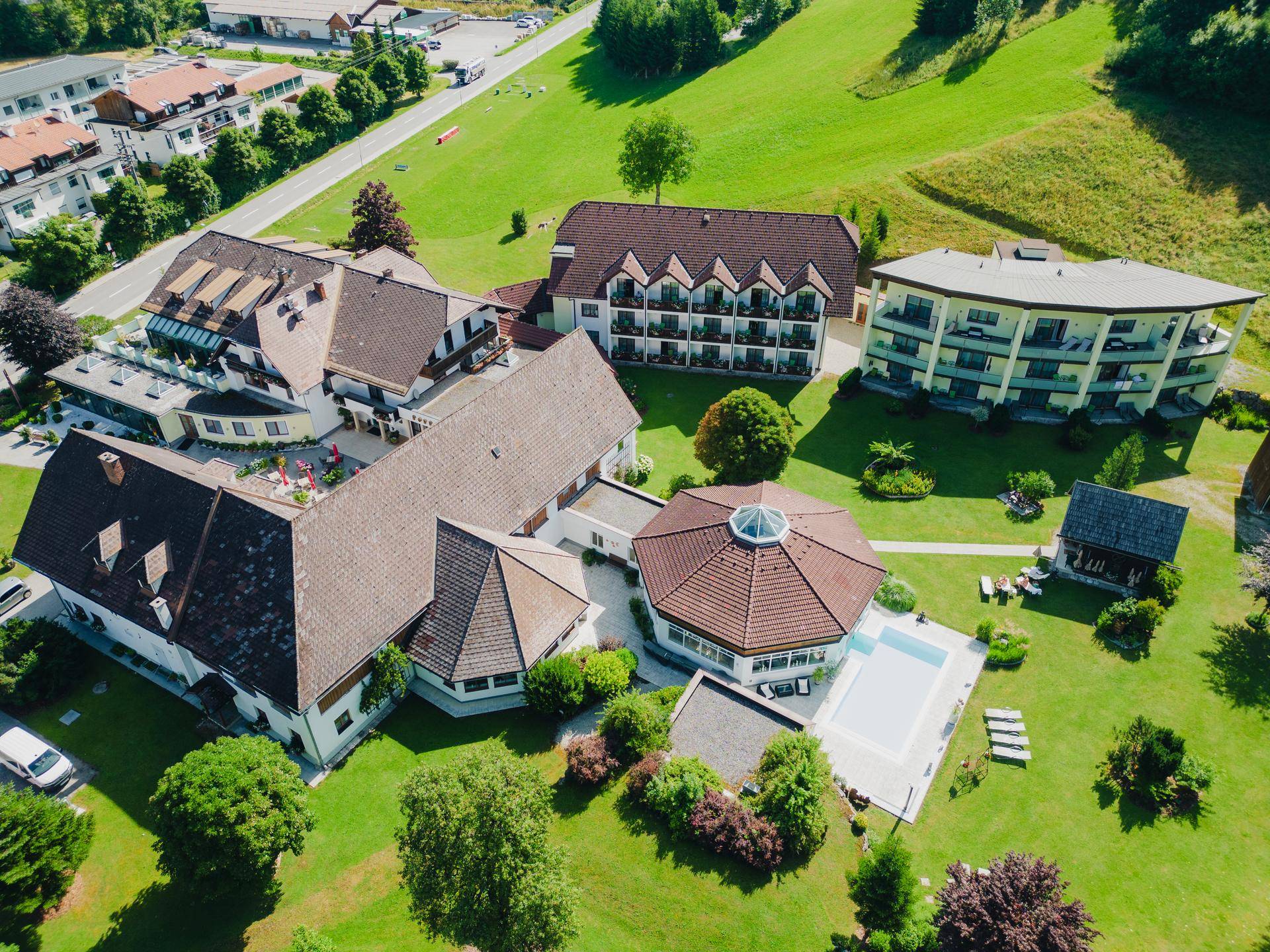Luftaufnahme eines weitläufigen Hotelkomplexes mit mehreren Gebäuden, Pool und grünen Wiesen.
