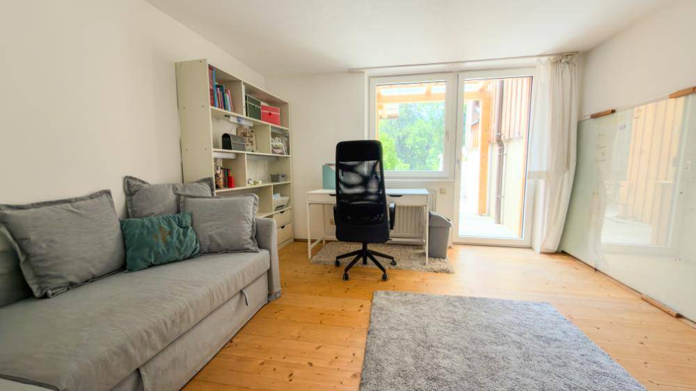 Helles Arbeitszimmer mit Schreibtisch, Sofa und Zugang zu einem Außenbereich.