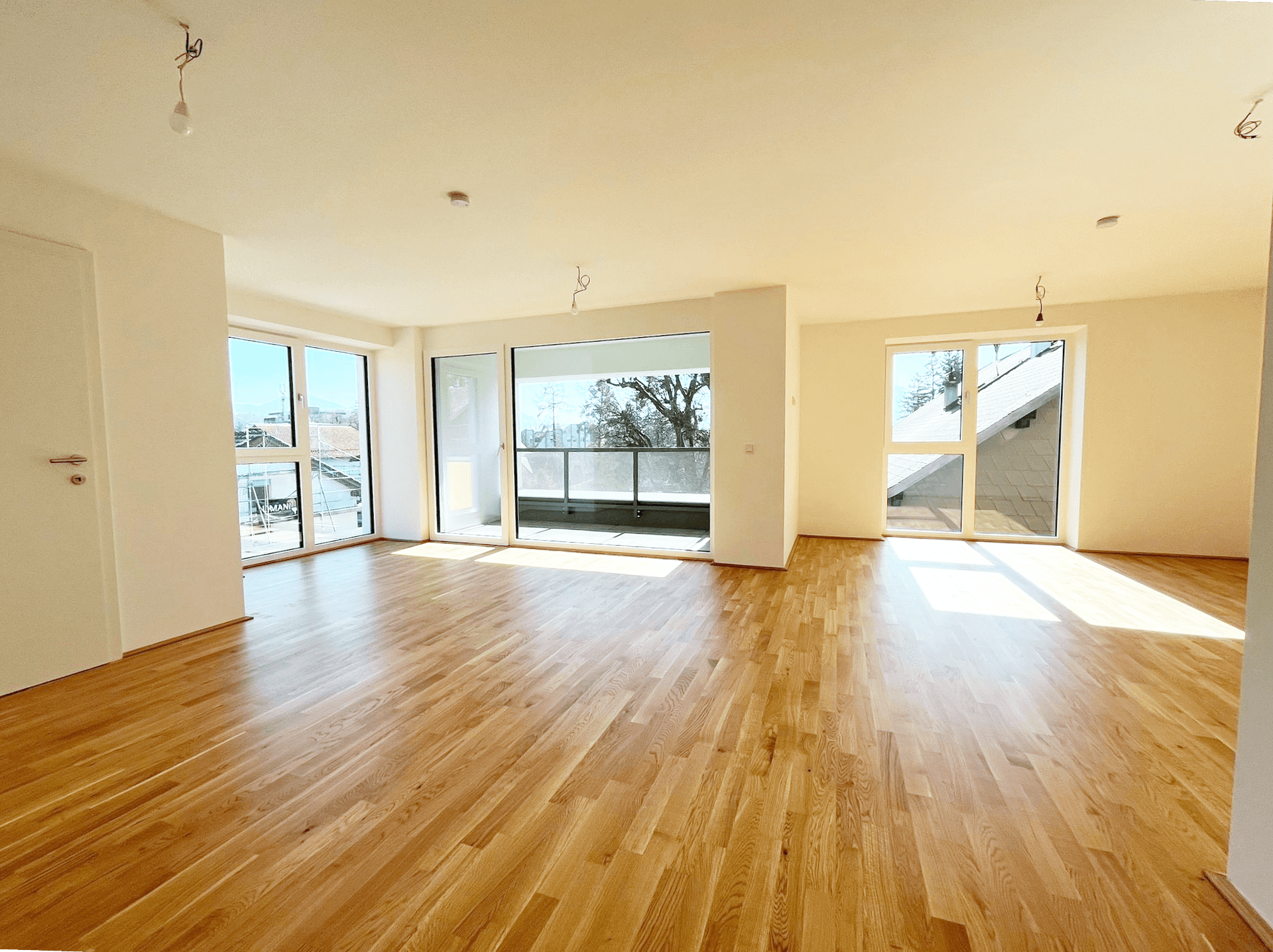 Heller, leerer Wohnbereich mit Holzboden und großen Fenstern, die Zugang zu einem Balkon bieten.