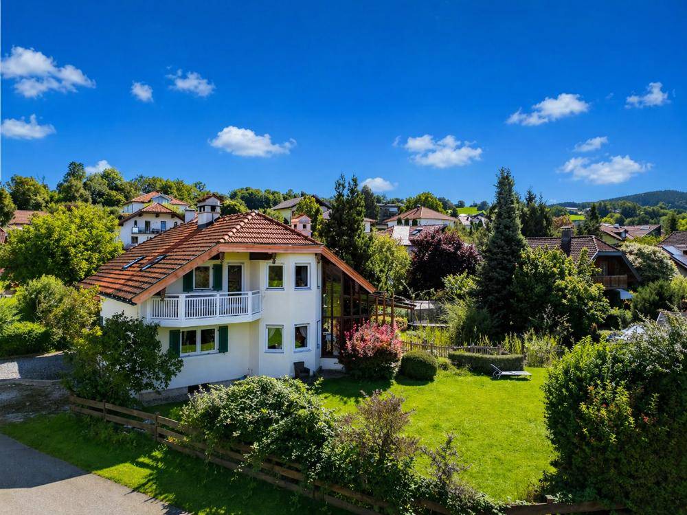 Luftaufnahme eines charmanten Hauses mit Garten und umliegender Wohnbebauung in grüner Umgebung.