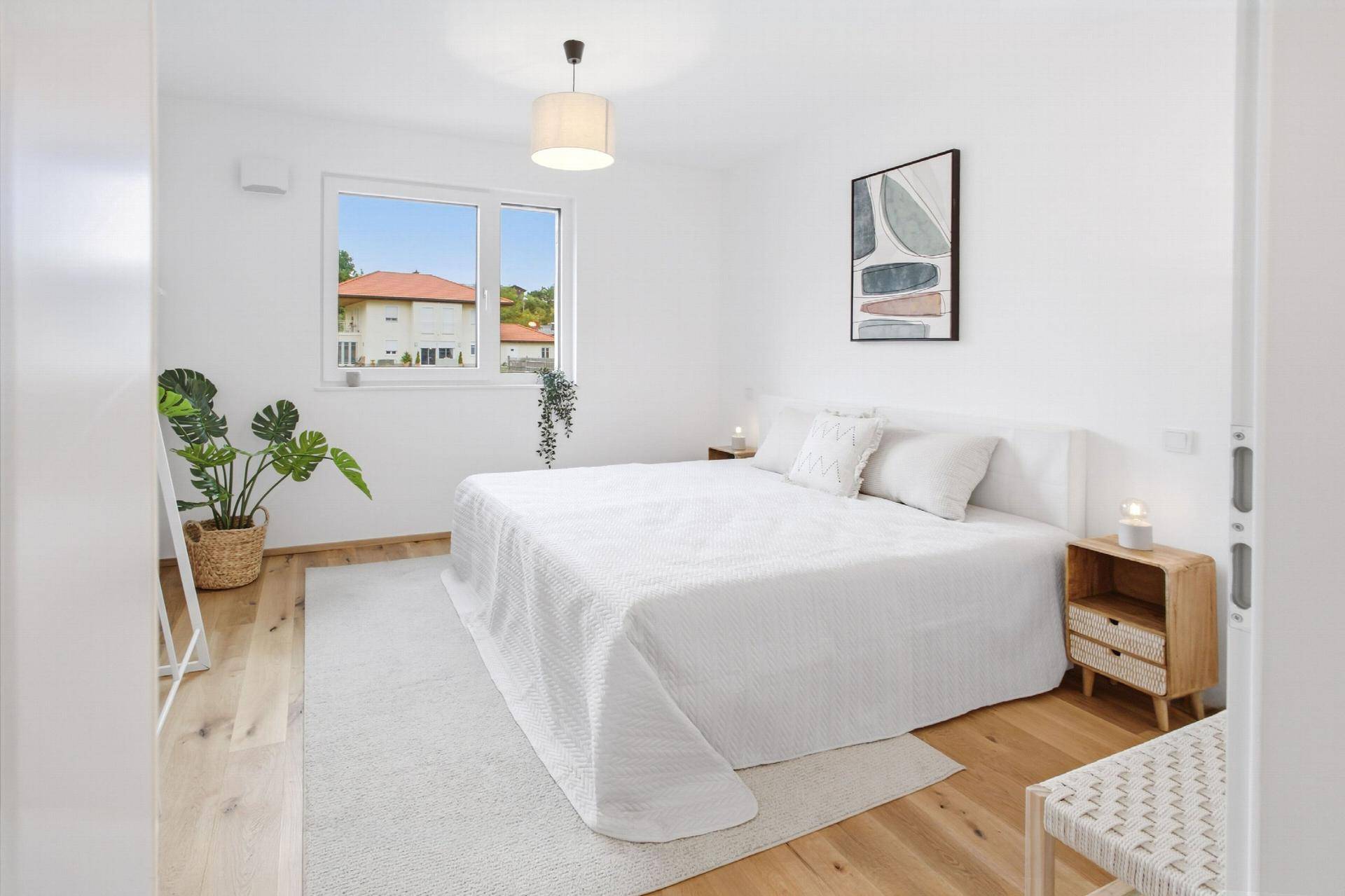 Helles Schlafzimmer mit großem Doppelbett, Holzboden und Blick ins Grüne.