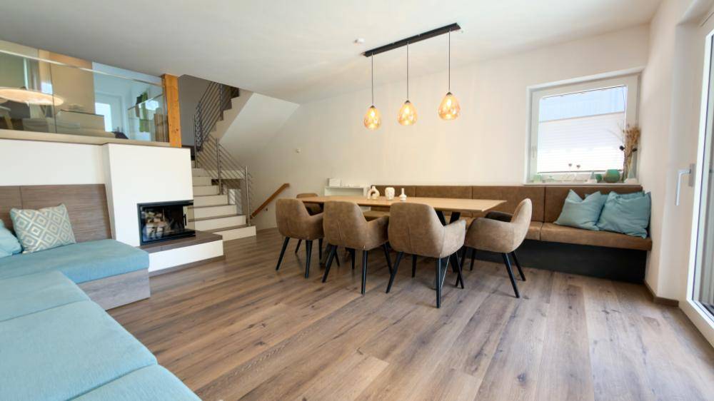 Heller Wohn- und Essbereich mit Holzboden, Kamin und offener Treppe zum Obergeschoss.