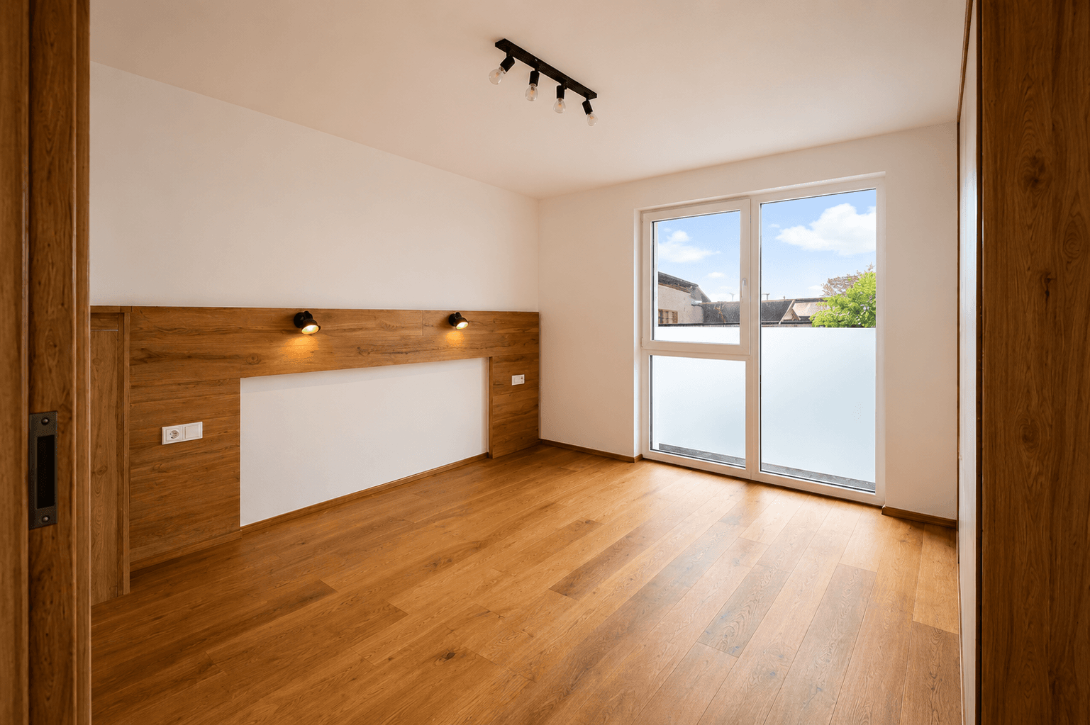Schlafzimmer mit Holzboden, weiß gestrichenen Wänden und Zugang zu einem privaten Außenbereich.