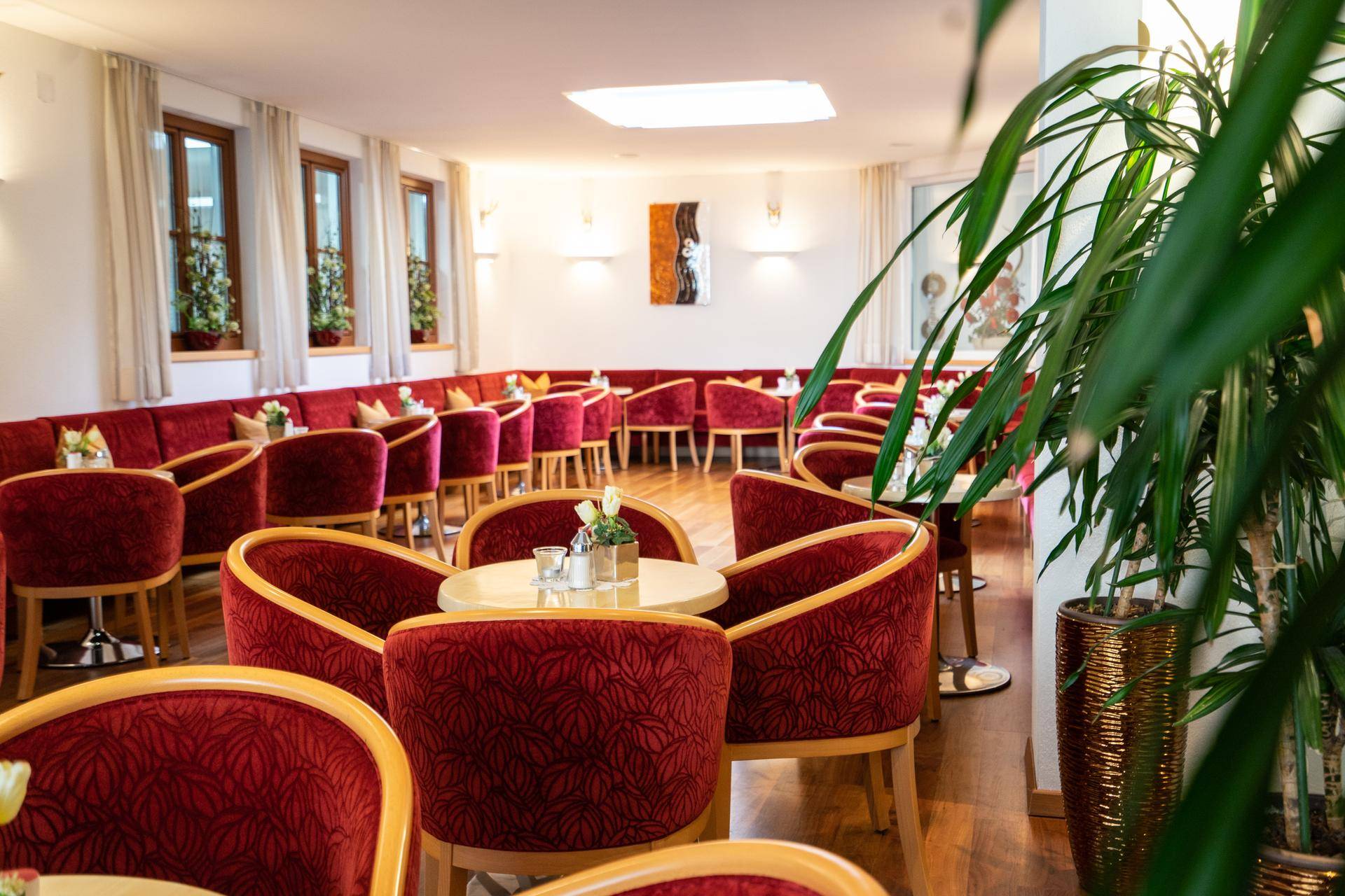 Eleganter Speisesaal mit zahlreichen roten Samtstühlen und kleinen Tischen, hell beleuchtet.