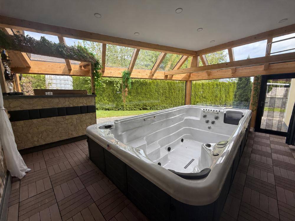 Überdachter Wellnessbereich mit großem Whirlpool und Blick in den Garten.