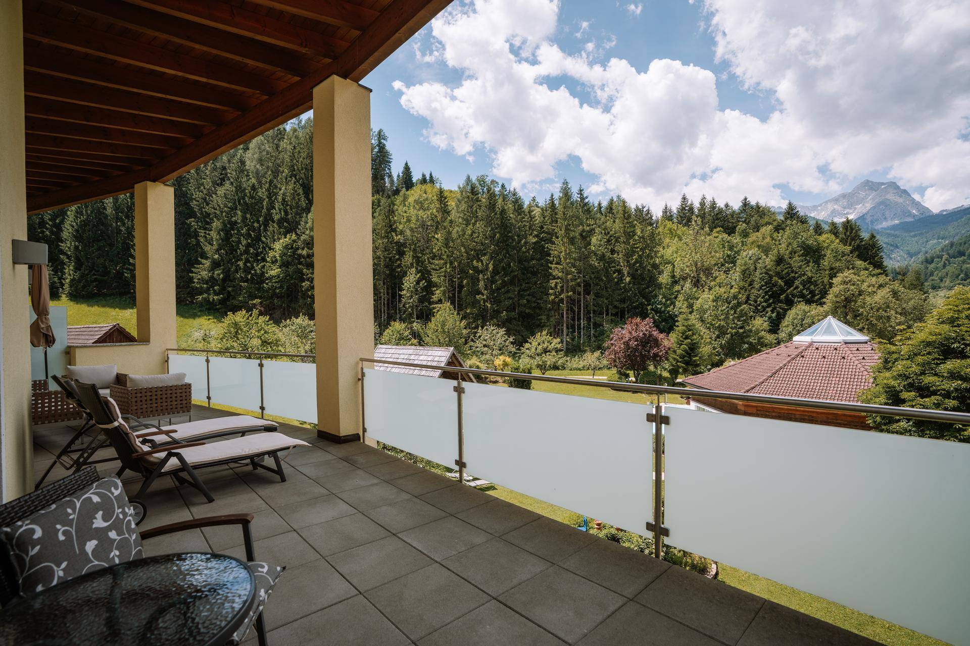 Geräumiger Balkon mit Liegestühlen und Tisch, bietet einen weiten Blick auf Wald und Berge.