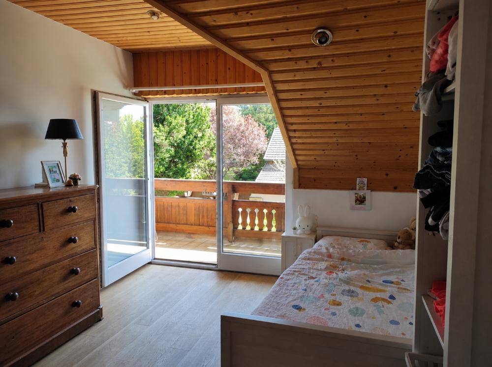 Schlafzimmer mit Holzbalkendecke, Holzkommode und direktem Zugang zu einem Balkon mit Aussicht.