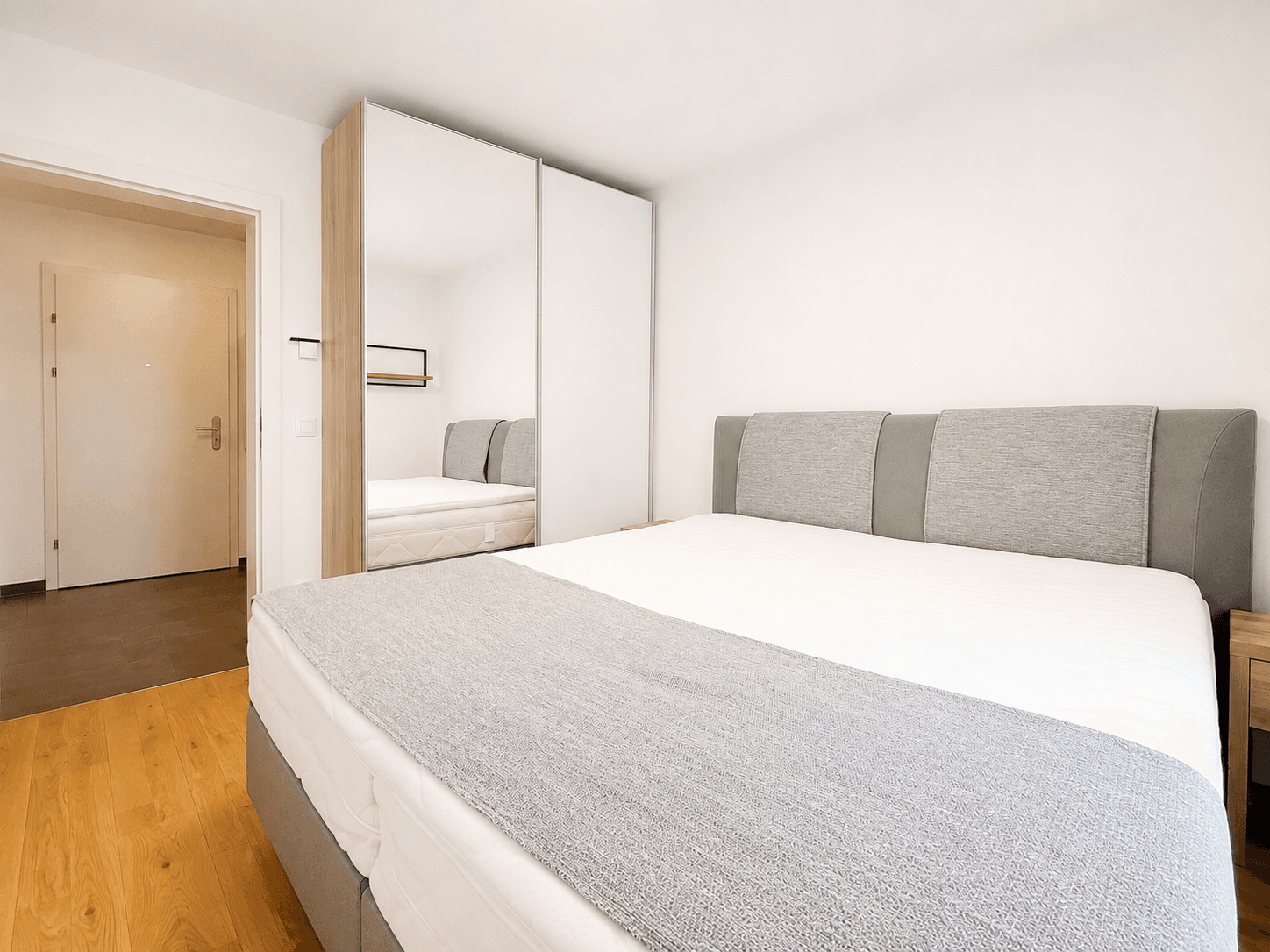 Schlafzimmer mit Doppelbett, Spiegelschrank und hellem Holzboden, bietet Komfort und Stauraum.