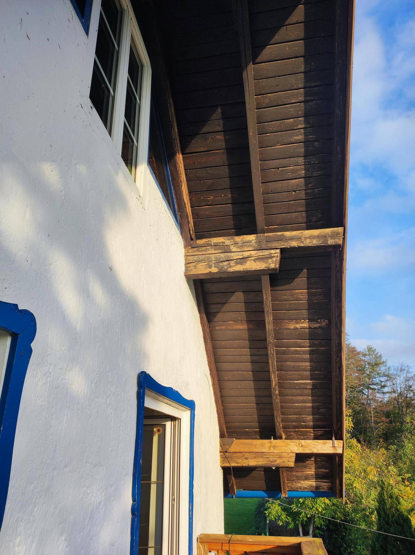 Detailansicht der weißen Hausfassade mit blauen Fensterrahmen und dunkler Holzverkleidung unter dem Dach.