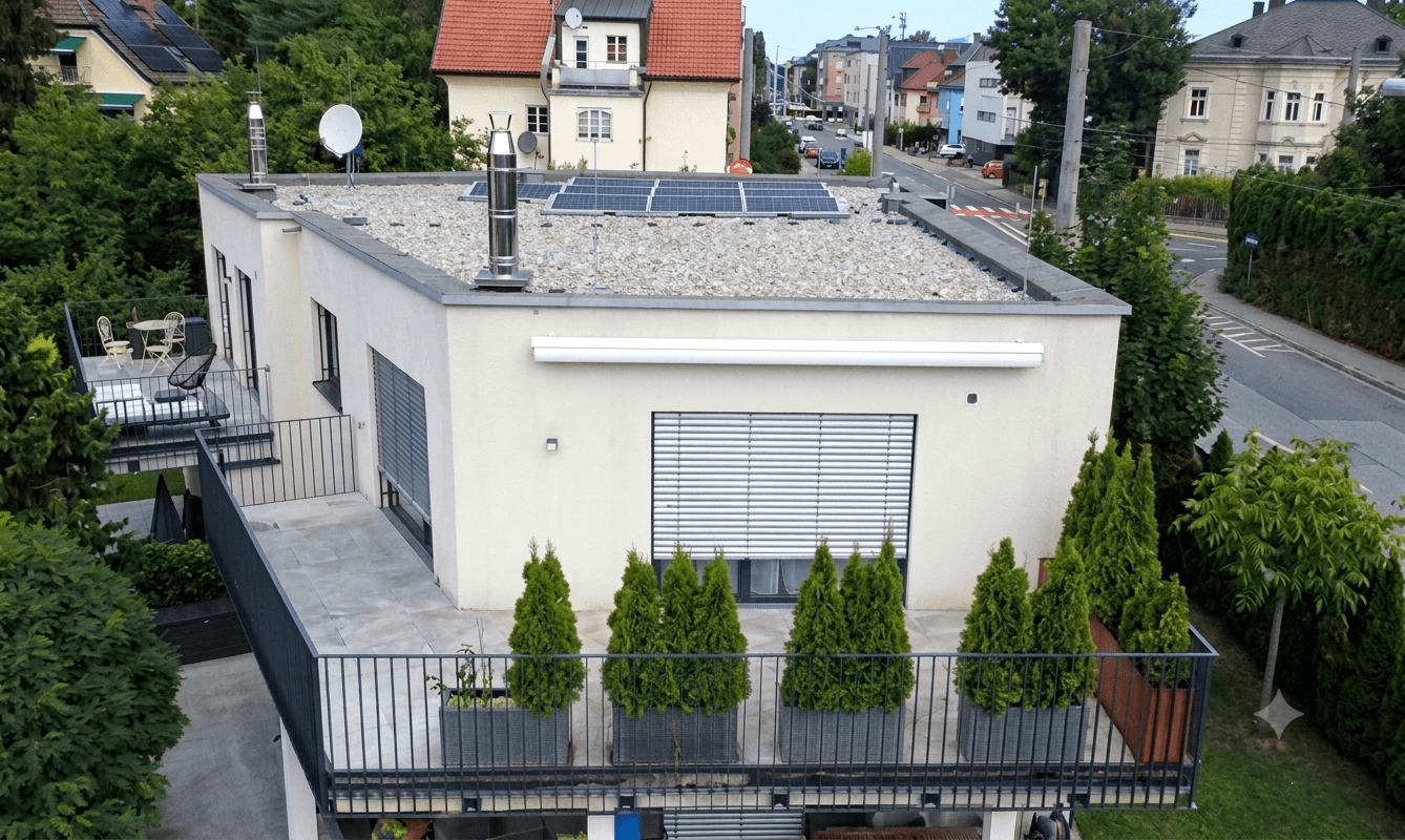 Luftaufnahme eines modernen Gebäudes mit Flachdach, Solaranlage und großer Terrasse.