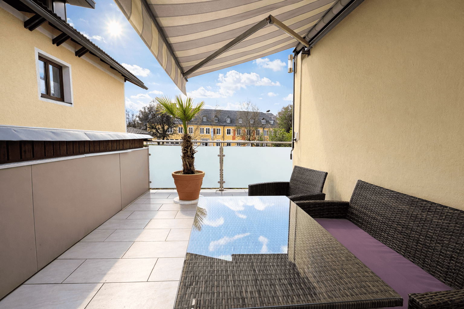 Sonniger Balkon mit Markise, Outdoor-Möbeln und Blick auf die Umgebung.