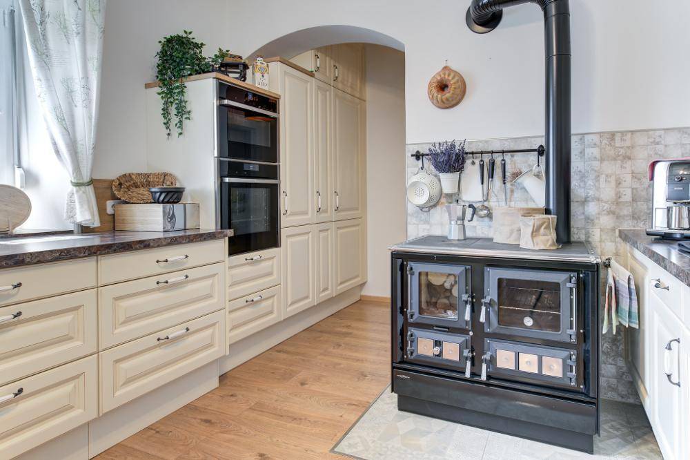 Landhausküche mit modernem Backofen, integriertem Holzofen und Fliesenboden.
