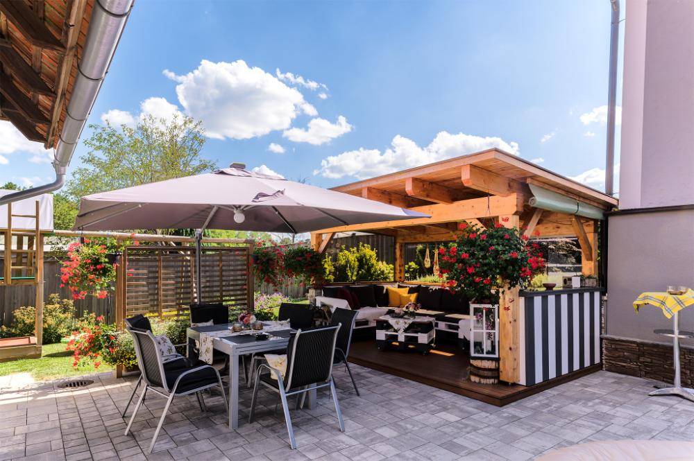 Überdachter Essbereich und Lounge-Ecke im gepflasterten Innenhof mit Blumen.