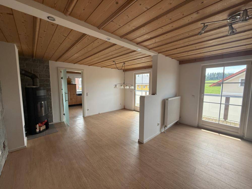 Geräumiges Wohnzimmer mit Holzbalkendecke, Kaminofen und Zugang zum Balkon.