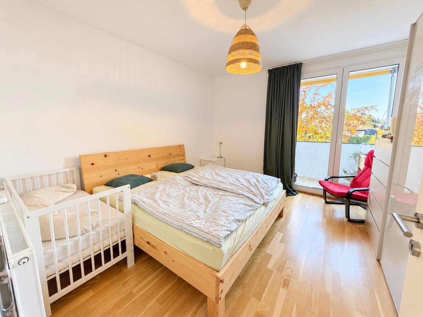 Helles Schlafzimmer mit Holzbett, Parkettboden und direktem Zugang zu einem Balkon.