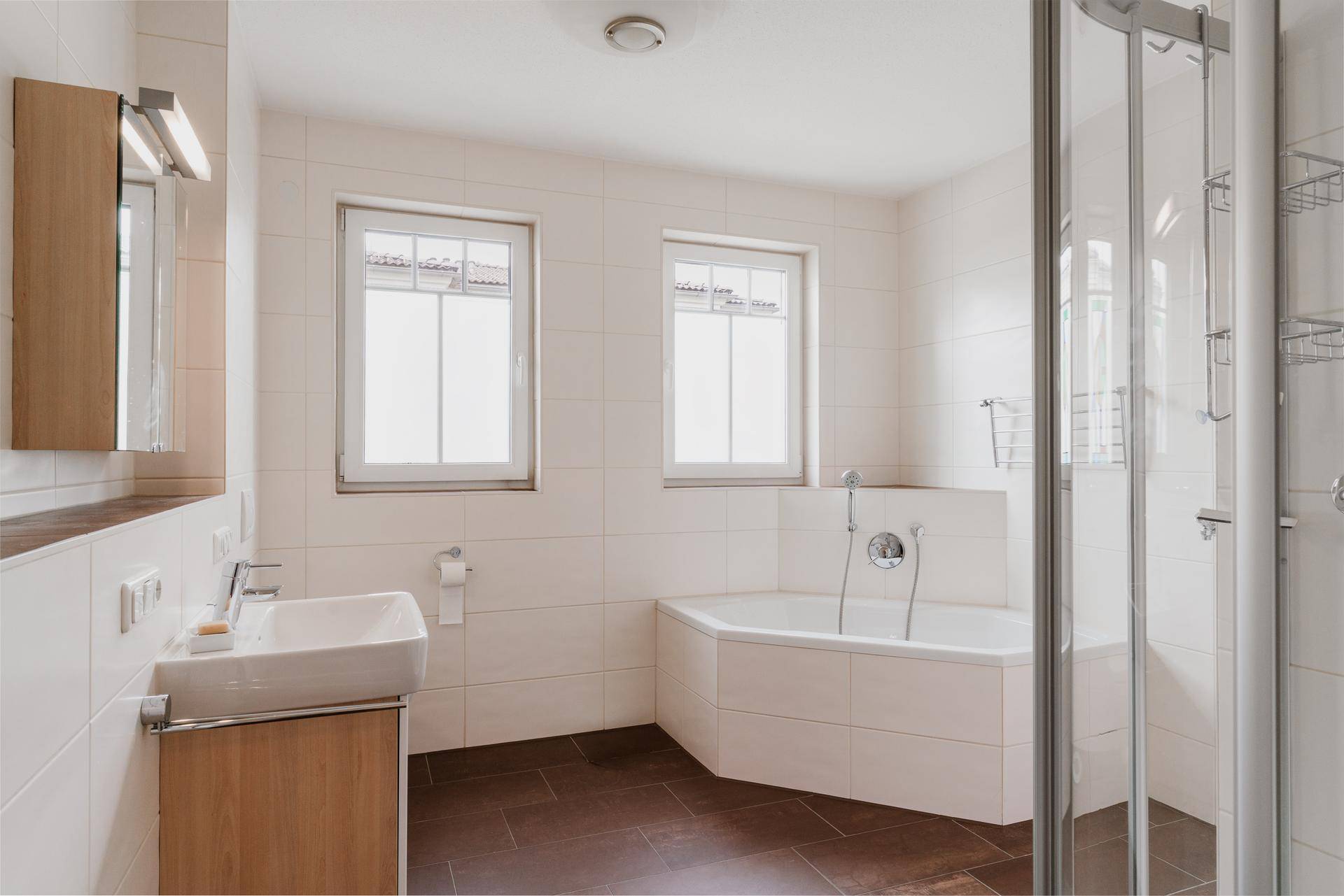 Geräumiges Badezimmer mit Badewanne, Dusche, Waschbecken und zwei Fenstern.