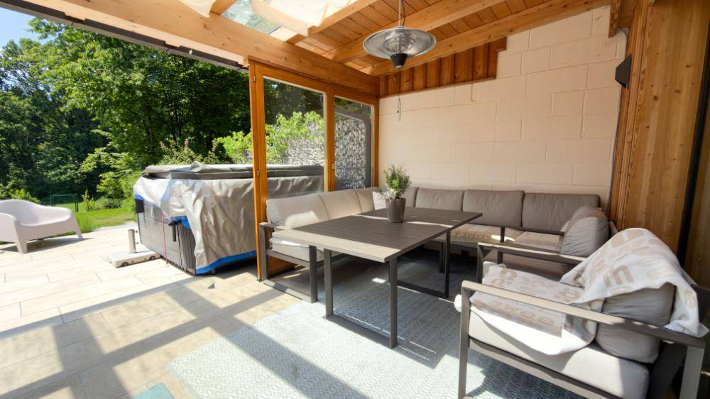 Überdachte Terrasse mit Sitzgelegenheiten, Whirlpool und Blick ins Grüne.