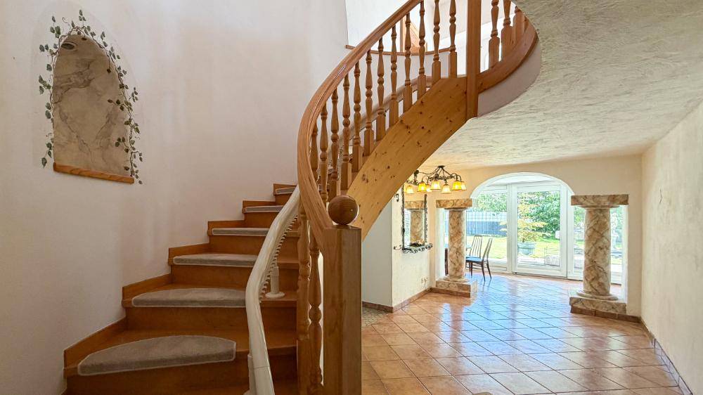 Elegante Holzwendeltreppe im Flur mit Terrakottafliesen und Zugang zum Garten.