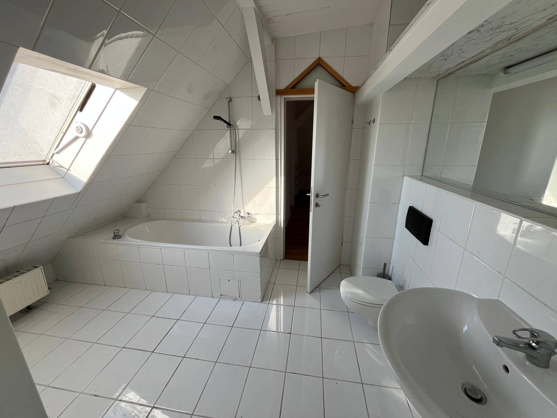 Helles Badezimmer im Dachgeschoss mit weißen Fliesen, Badewanne und praktischem Dachfenster.