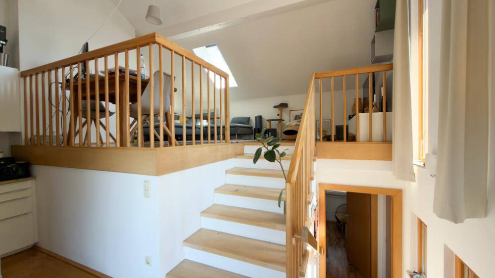 Offener Treppenbereich mit Holzgeländer, der zu einem hellen Loft-Wohnbereich führt.