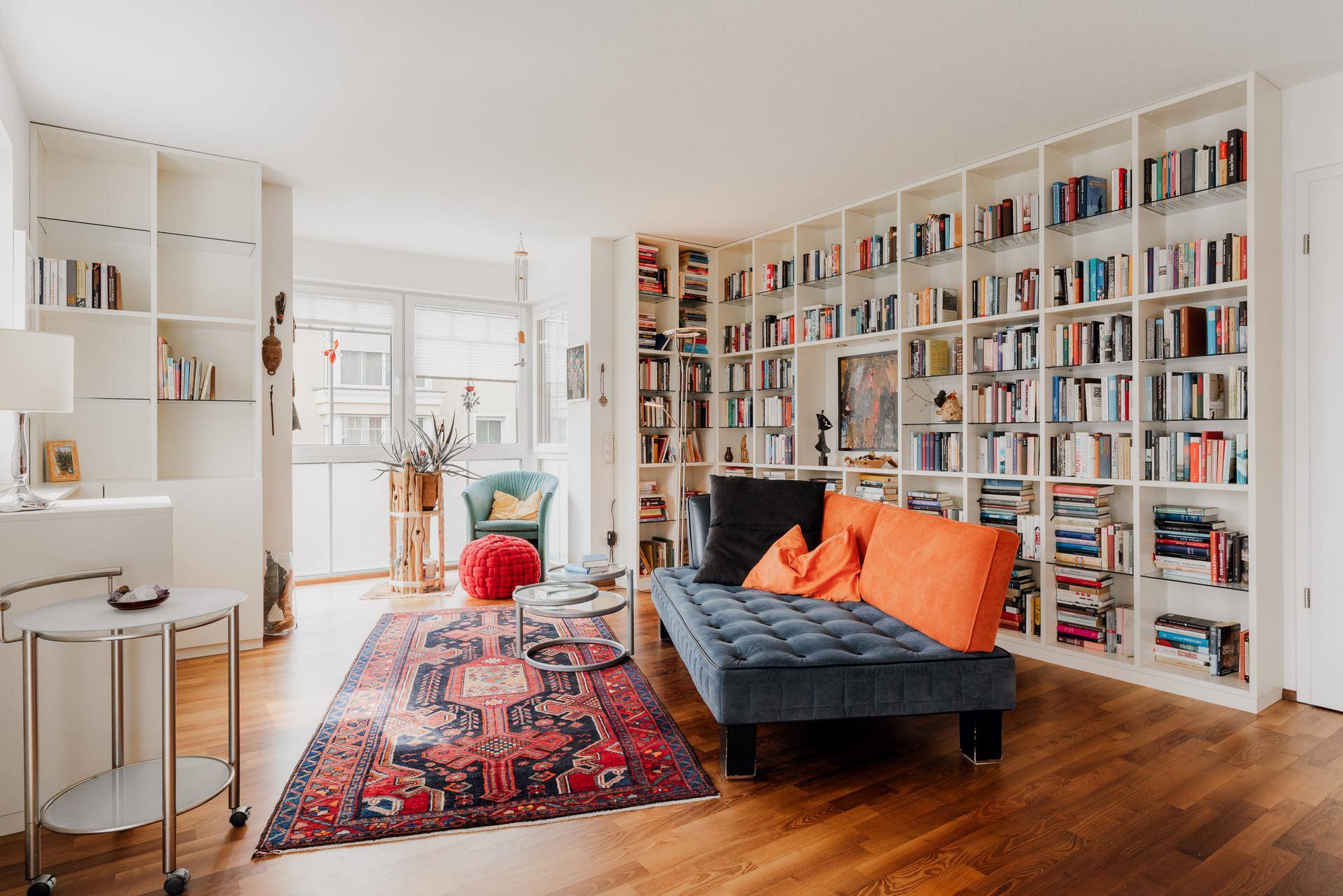 Helles Wohnzimmer mit großer Bücherwand, Holzboden und gemütlicher Sitzecke.