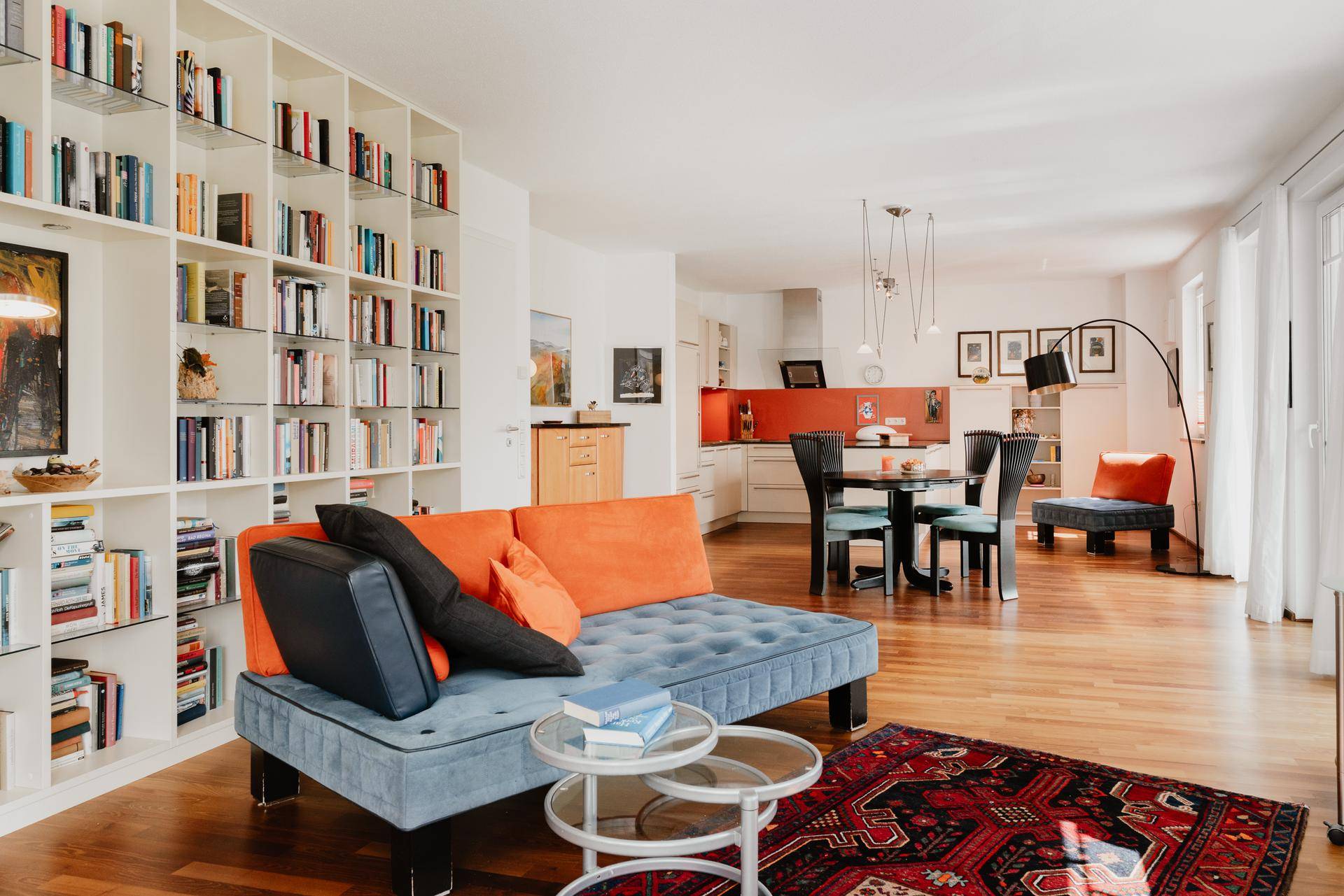 Offener Wohn- und Essbereich mit Holzboden, Bücherwand und Blick zur Küche.