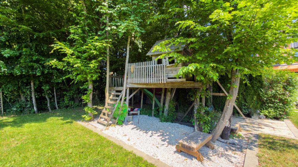Kinderspielbereich im Garten mit einem charmanten Baumhaus und viel Grün.