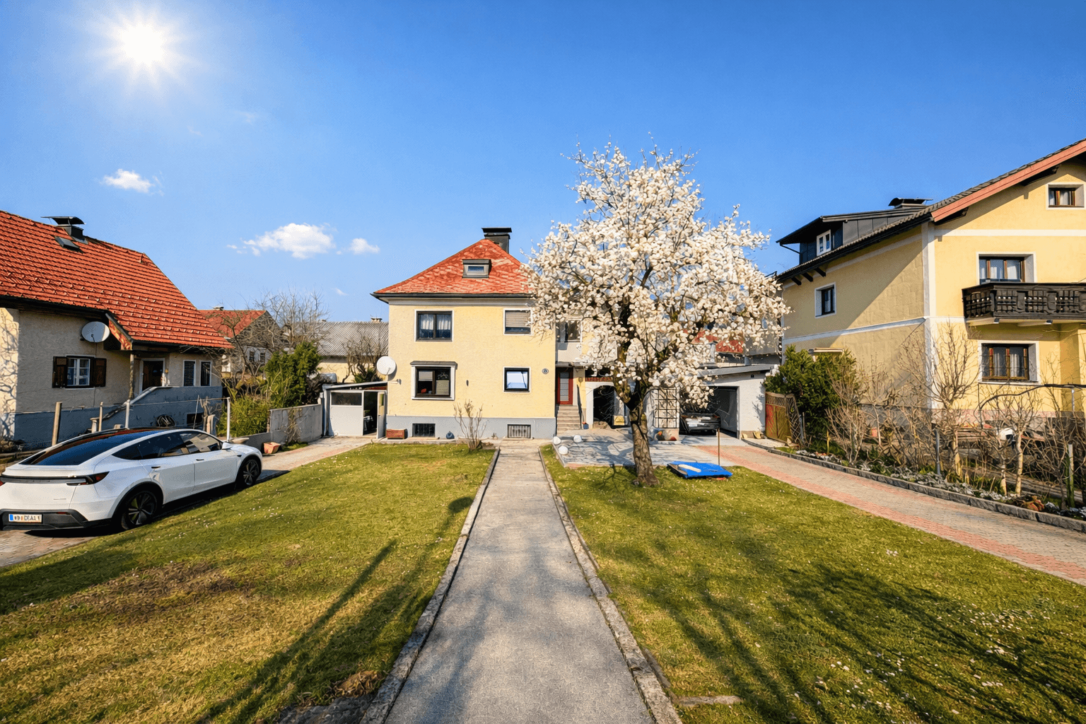 Einfamilienhaus mit großem Vorgarten, blühendem Baum und sonnigem Wetter.