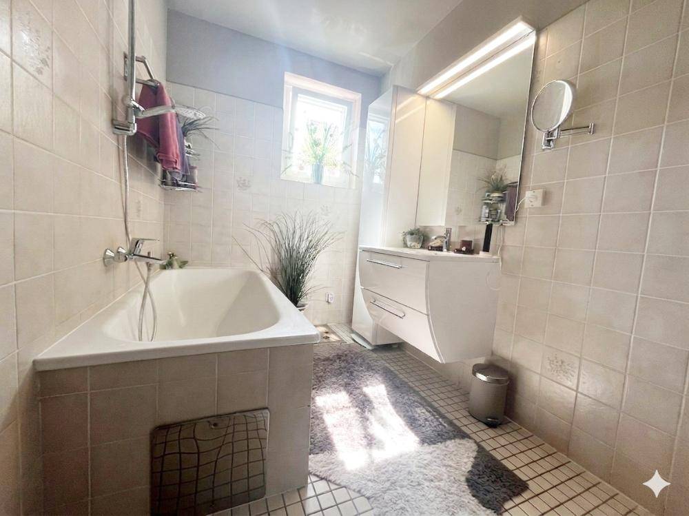 Gefliestes Badezimmer mit Eckbadewanne, Fenster und Spiegelschrank.