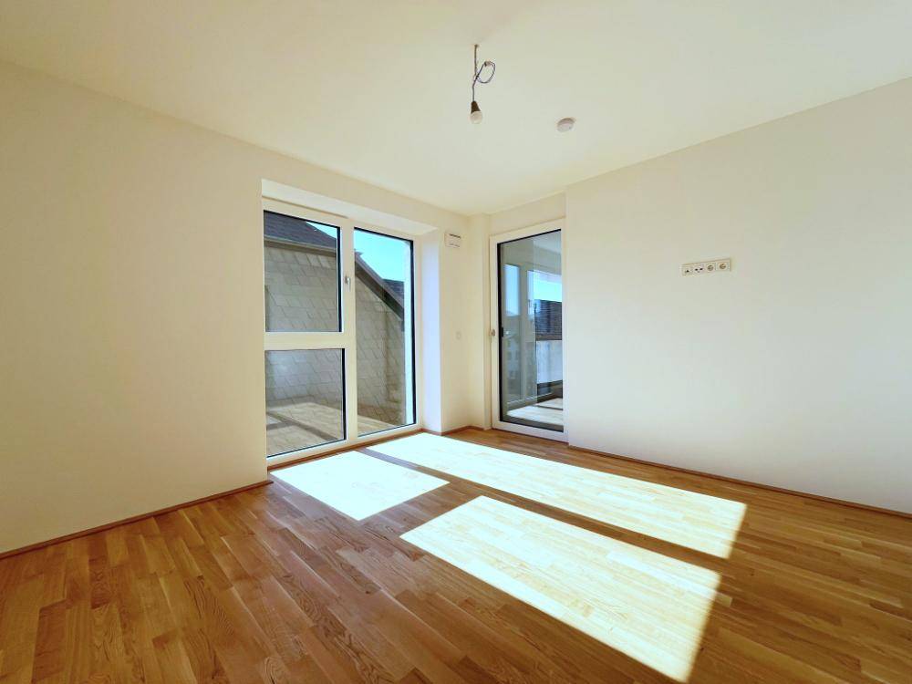 Helles Zimmer mit Holzboden und Zugang zu einem kleinen Balkon oder einer Terrasse.