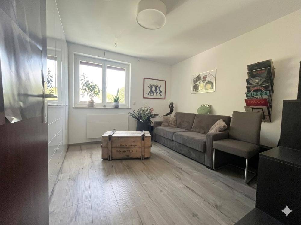 Helles Wohnzimmer mit Sofa, Schrankwand und Fenster mit Blick ins Grüne.
