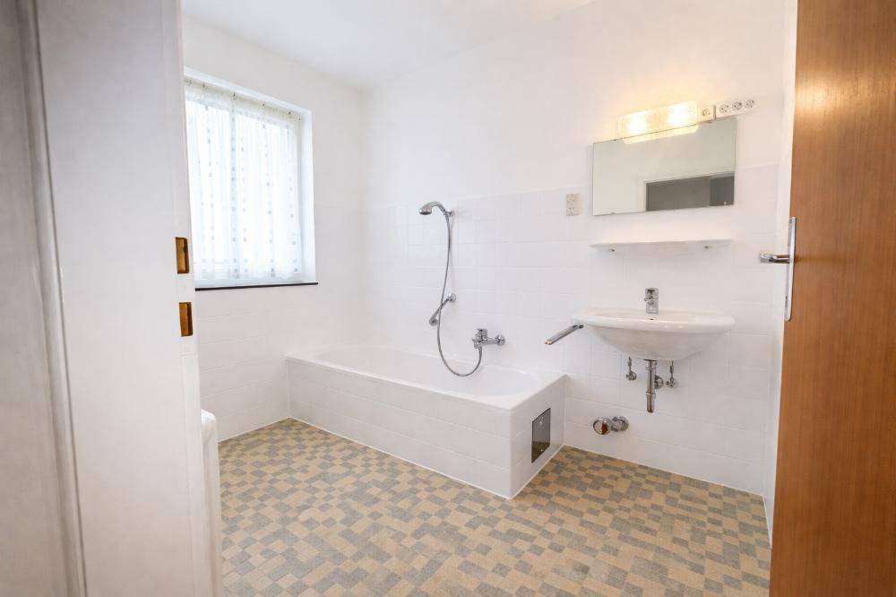 Helles Badezimmer mit Badewanne, Waschbecken und Fenster, ausgestattet mit hellen Fliesen.