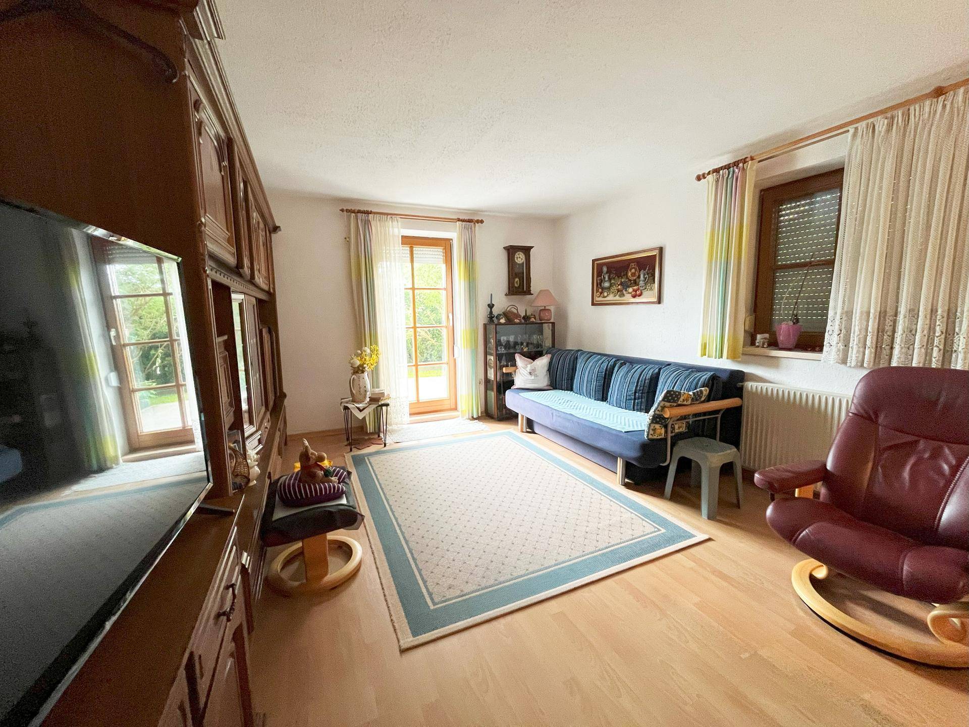 Gemütliches Wohnzimmer mit blauem Sofa, Holzmöbeln und Zugang zu einem Außenbereich.