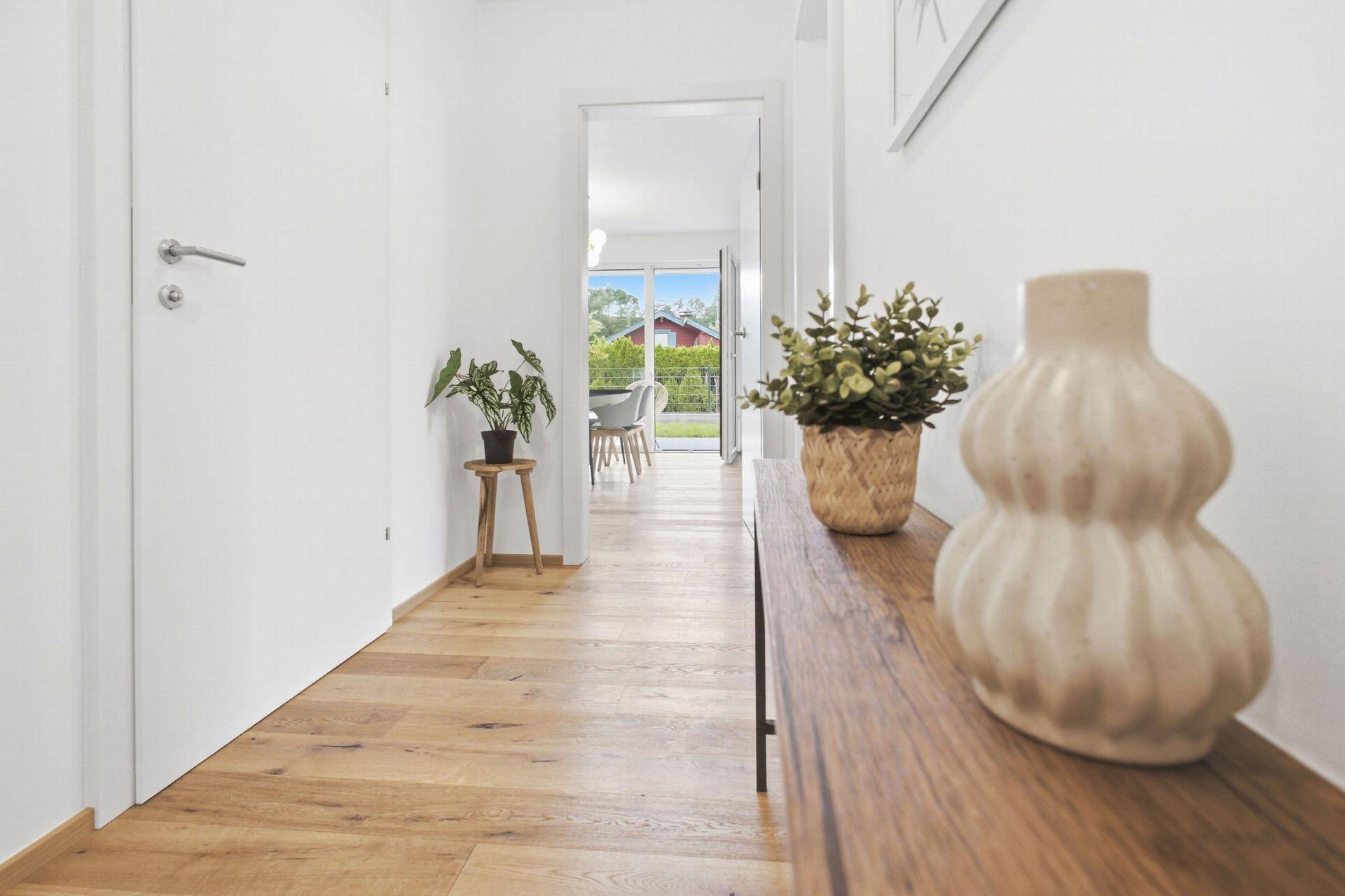 Heller Flur mit Holzboden, weiß gestrichenen Wänden und Blick in den Wohnbereich.