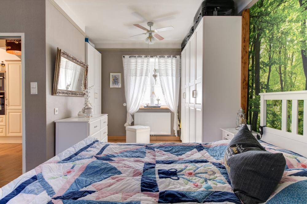 Komfortables Schlafzimmer mit Holzboden, großen Fenstern und Blick in die Küche.
