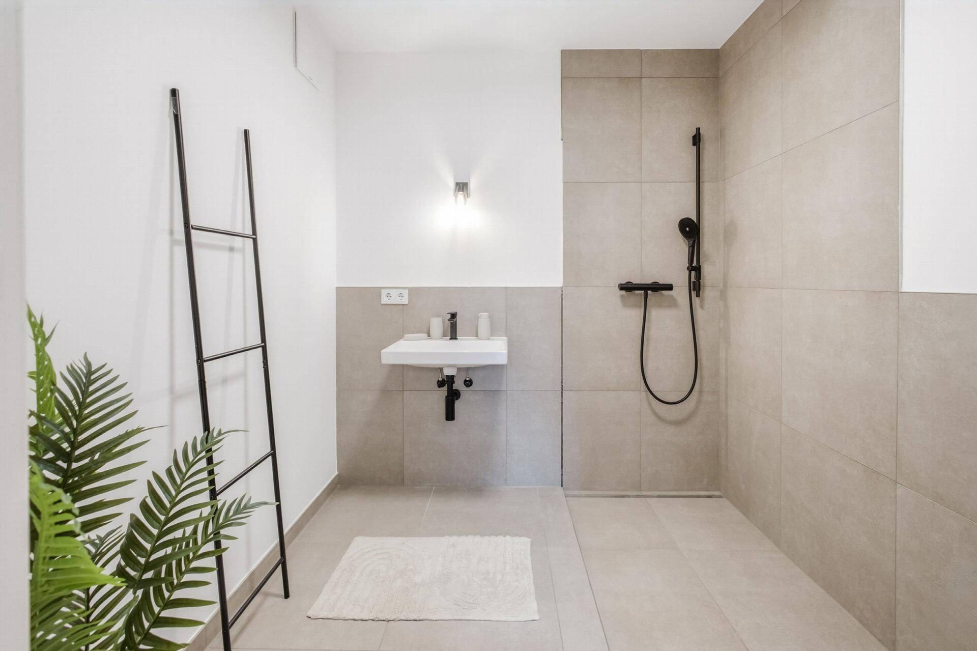 Modernes Badezimmer mit ebenerdiger Dusche, Wandwaschbecken und hellen Fliesen.