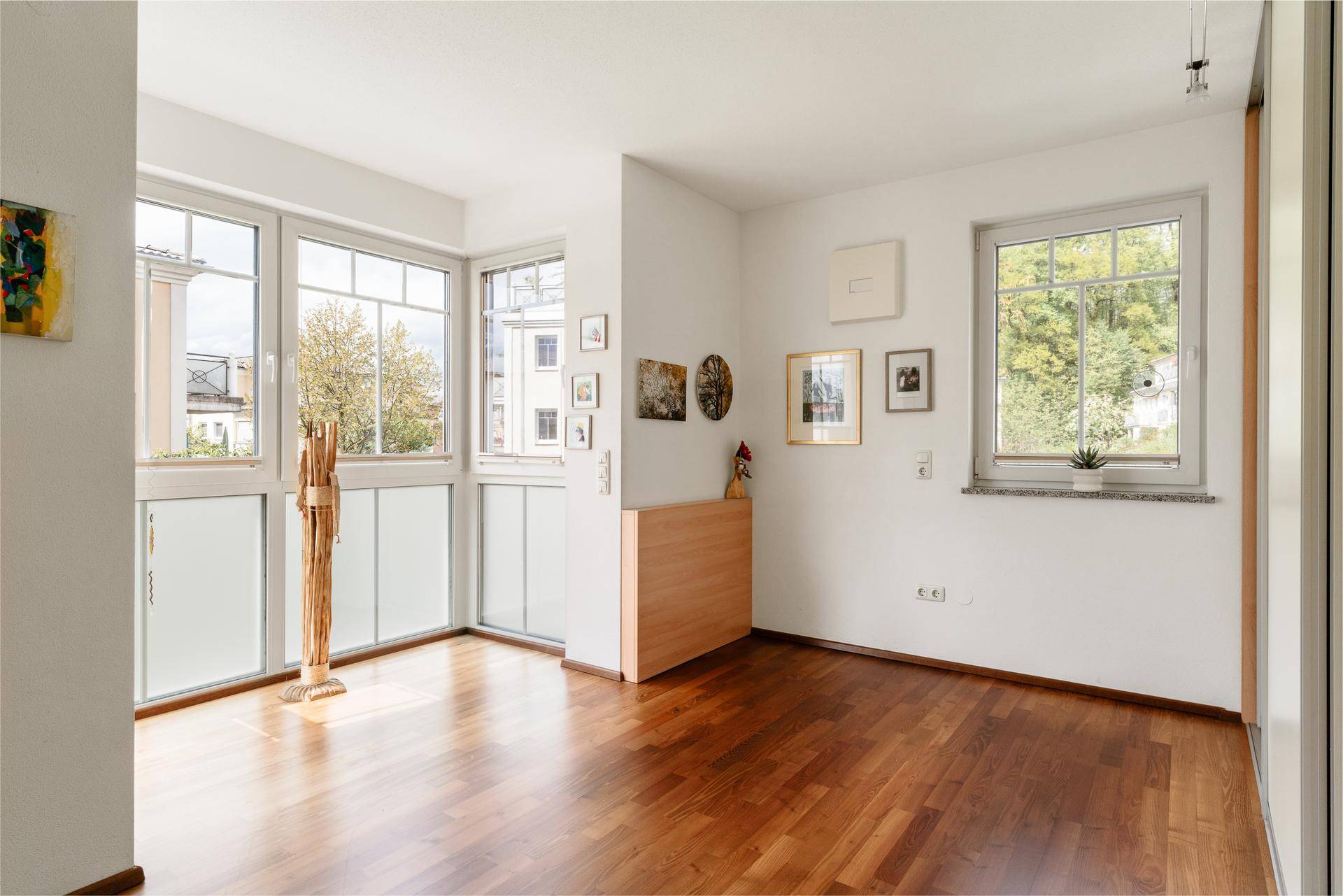 Heller Raum mit großen Fenstern, Holzboden und Zugang zu einem französischen Balkon.