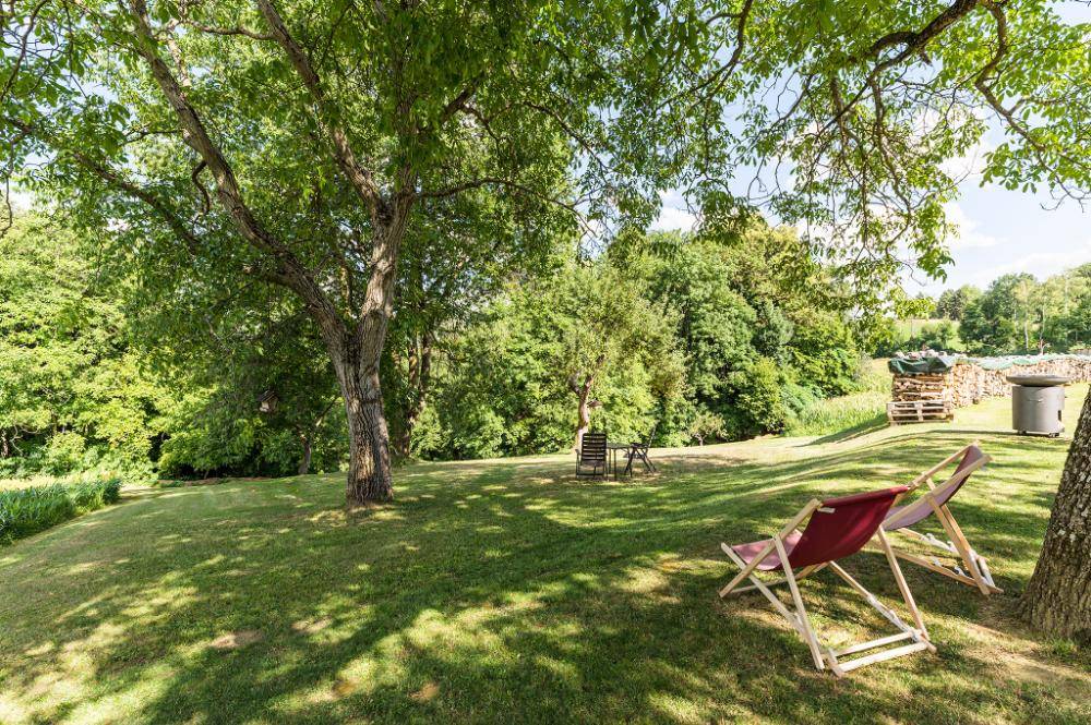 Großer, gepflegter Garten mit schattenspendenden Bäumen und Liegestühlen zum Entspannen.