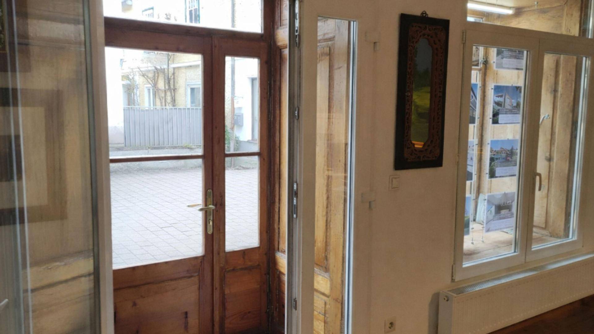 Eingangsbereich mit einer Holztür, die zu einem gepflasterten Innenhof führt, und großen Fenstern.