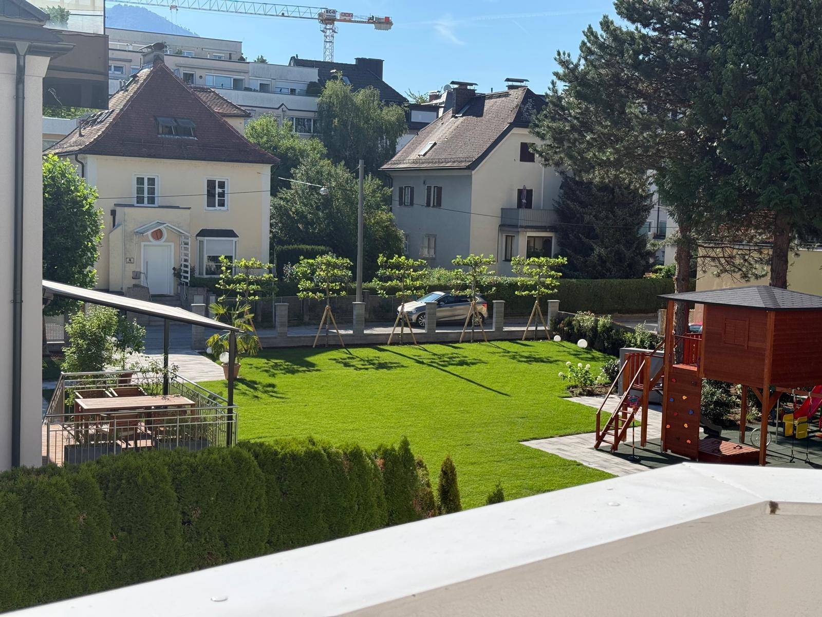 Gepflegter Gemeinschaftsgarten mit Rasenfläche, Spielplatz und Sitzbereich im Freien.
