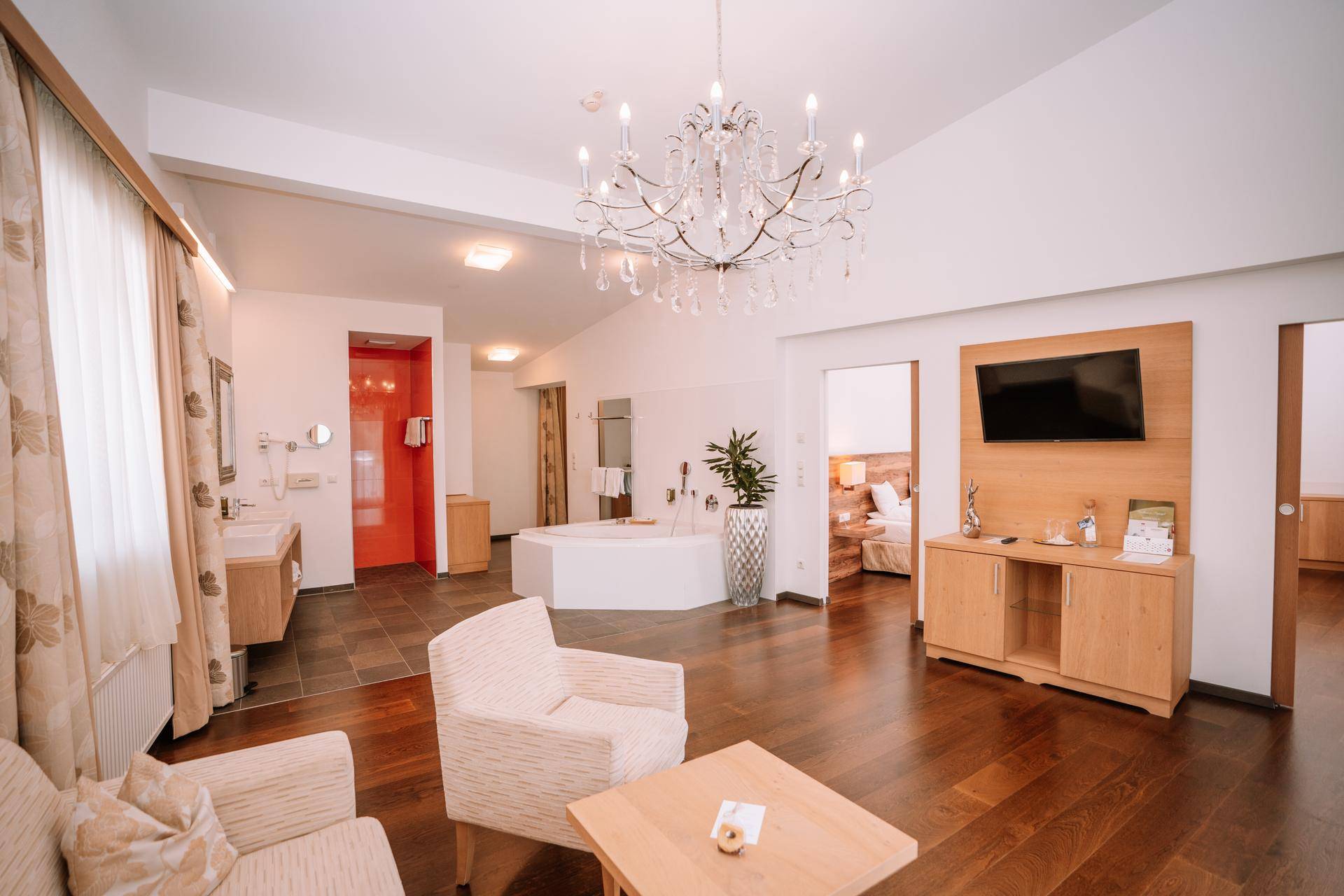 Helle Suite mit offenem Wohnbereich, Badewanne und Blick auf ein angrenzendes Schlafzimmer.
