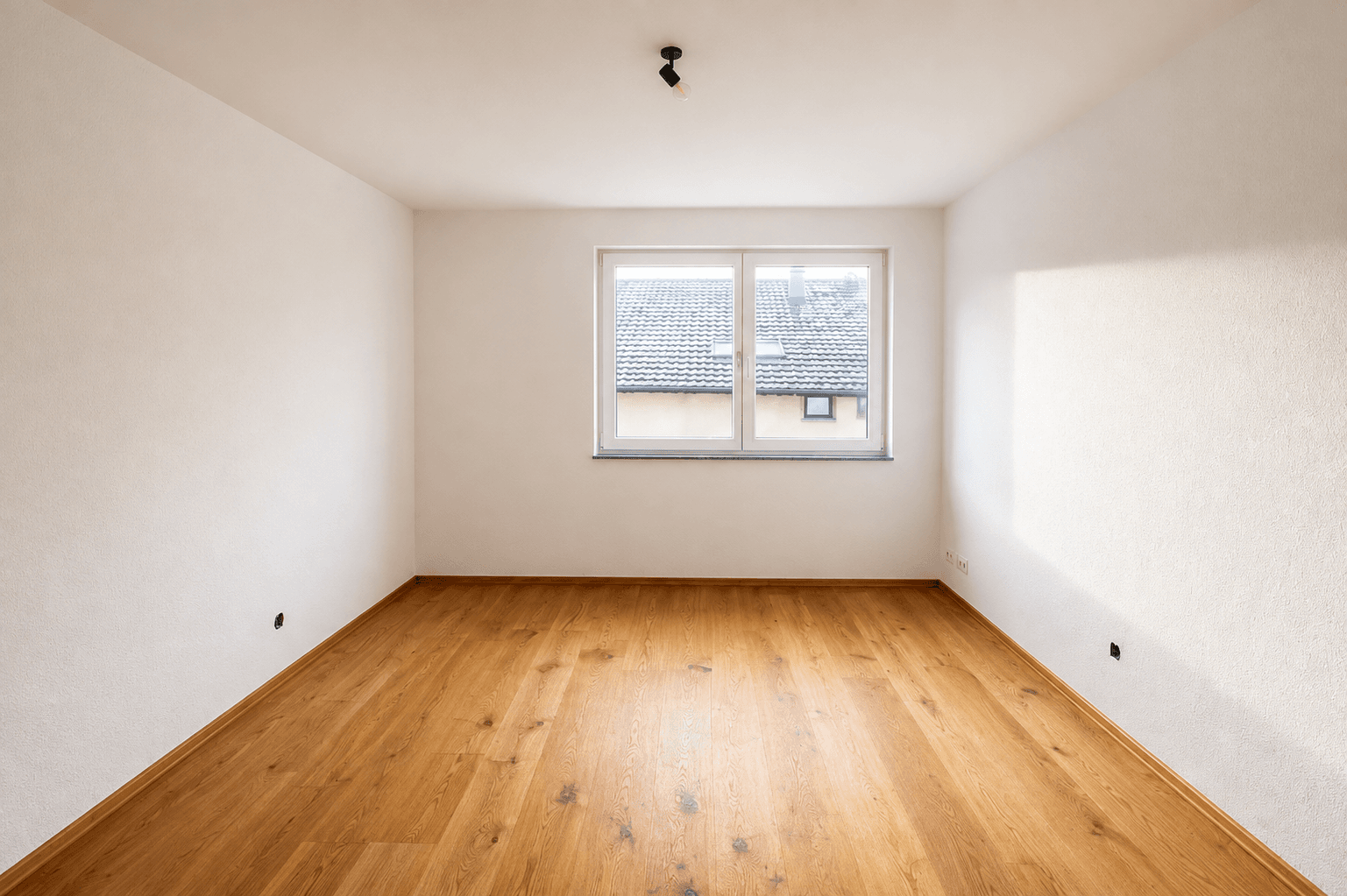 Helles Zimmer mit Holzboden und einem Fenster, ideal als Schlaf- oder Arbeitszimmer.