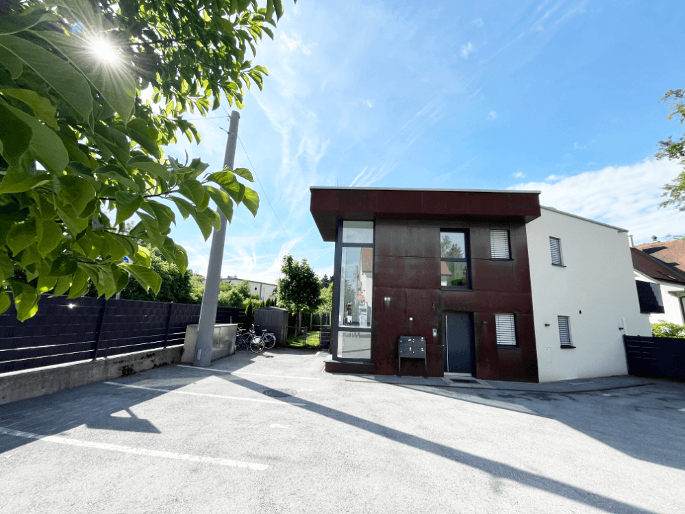 Moderne Architektur mit dunkler Fassade und großzügigem Parkplatz vor dem Gebäude.