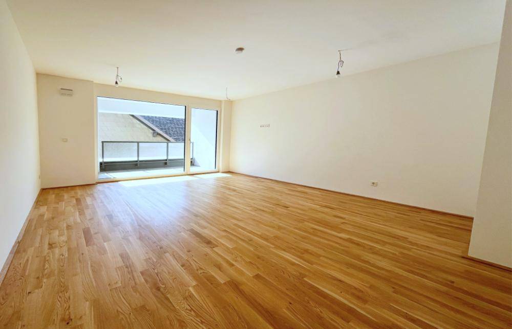 Großzügiger, unmöblierter Wohnbereich mit Parkettboden und breiter Schiebetür zum Balkon.