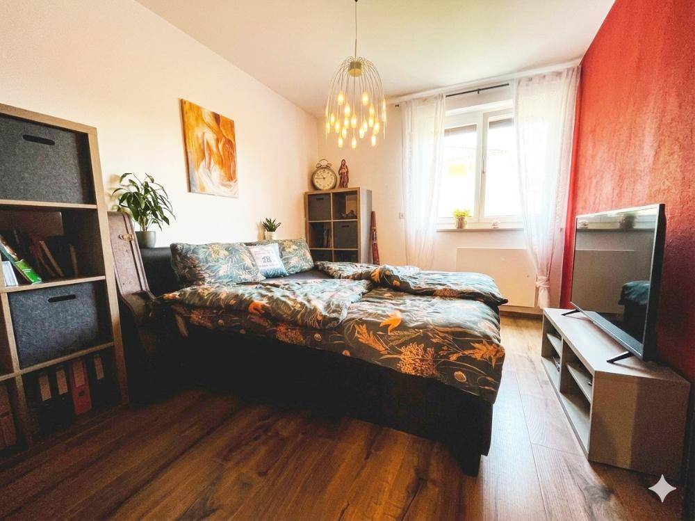 Gemütliches Schlafzimmer mit Holzboden, roter Akzentwand und großem Fenster.